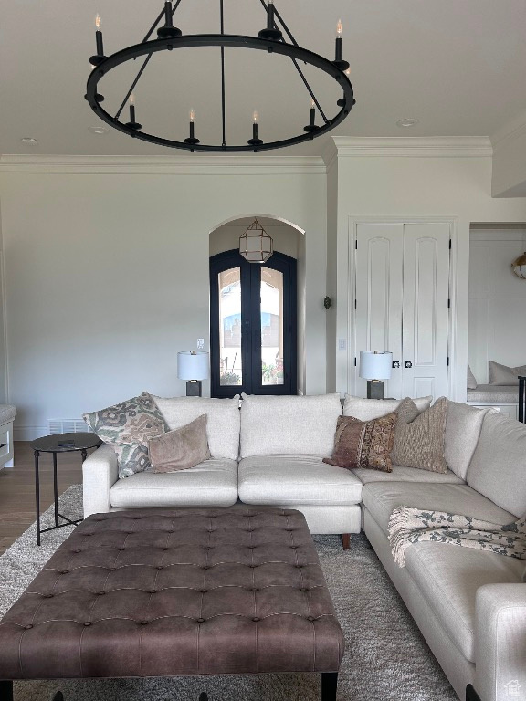 Living area with arched walkways, ornamental molding, a chandelier, french doors, and wood finished floors