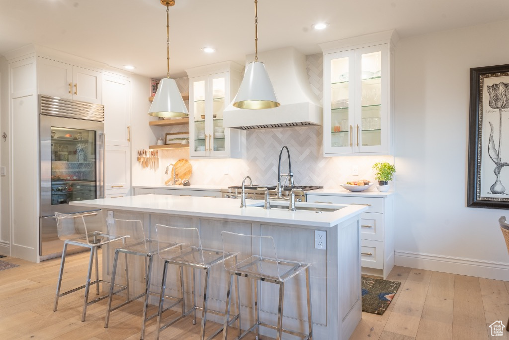 Kitchen with built in refrigerator, light countertops, a center island with sink, light wood finished floors, and white cabinets