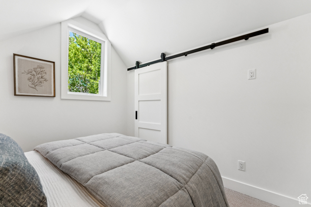 Bedroom featuring a barn door, carpet floors, and lofted ceiling