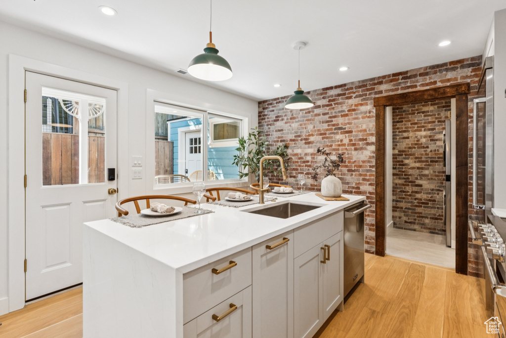 Kitchen featuring brick wall, stainless steel dishwasher, light wood finished floors, decorative light fixtures, and light countertops