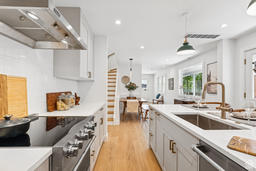 Kitchen featuring wall chimney range hood, appliances with stainless steel finishes, light wood-style floors, light countertops, and recessed lighting