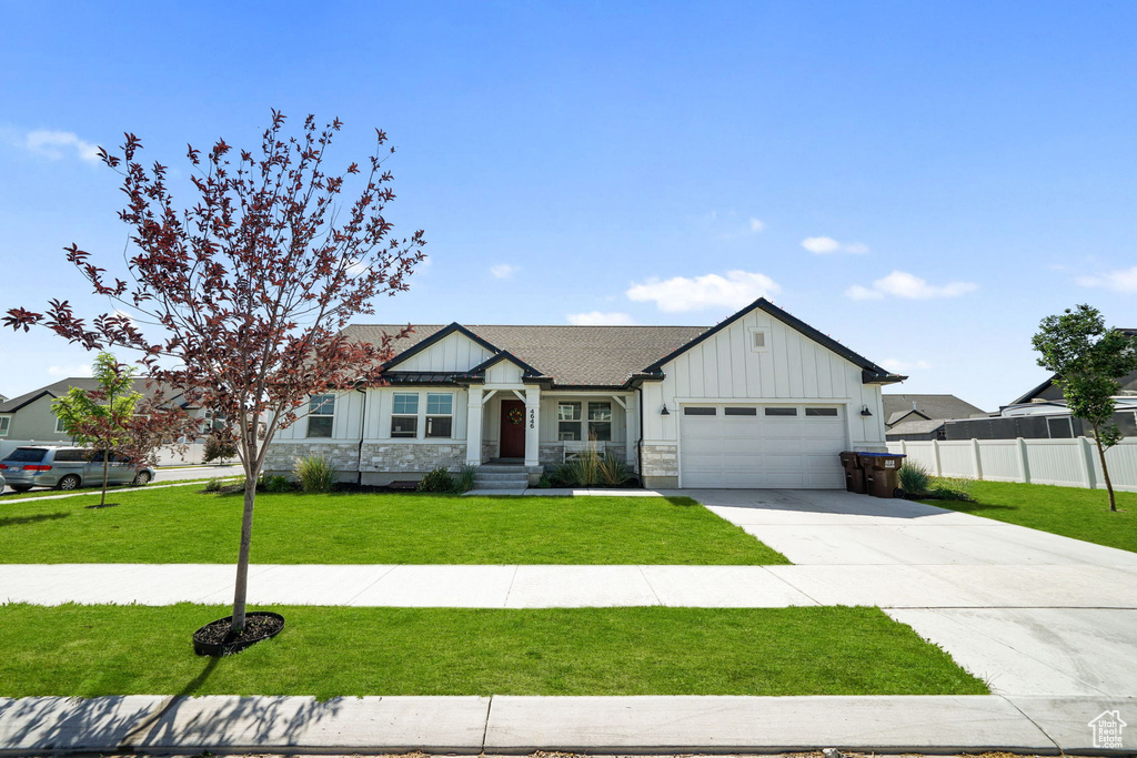 View of front facade with board and batten siding, an attached garage, driveway, and stone siding