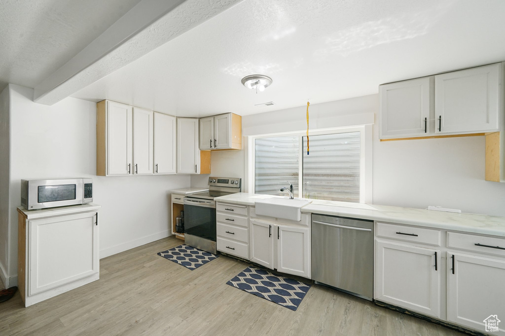 Kitchen featuring appliances with stainless steel finishes, light wood-type flooring, and white cabinets