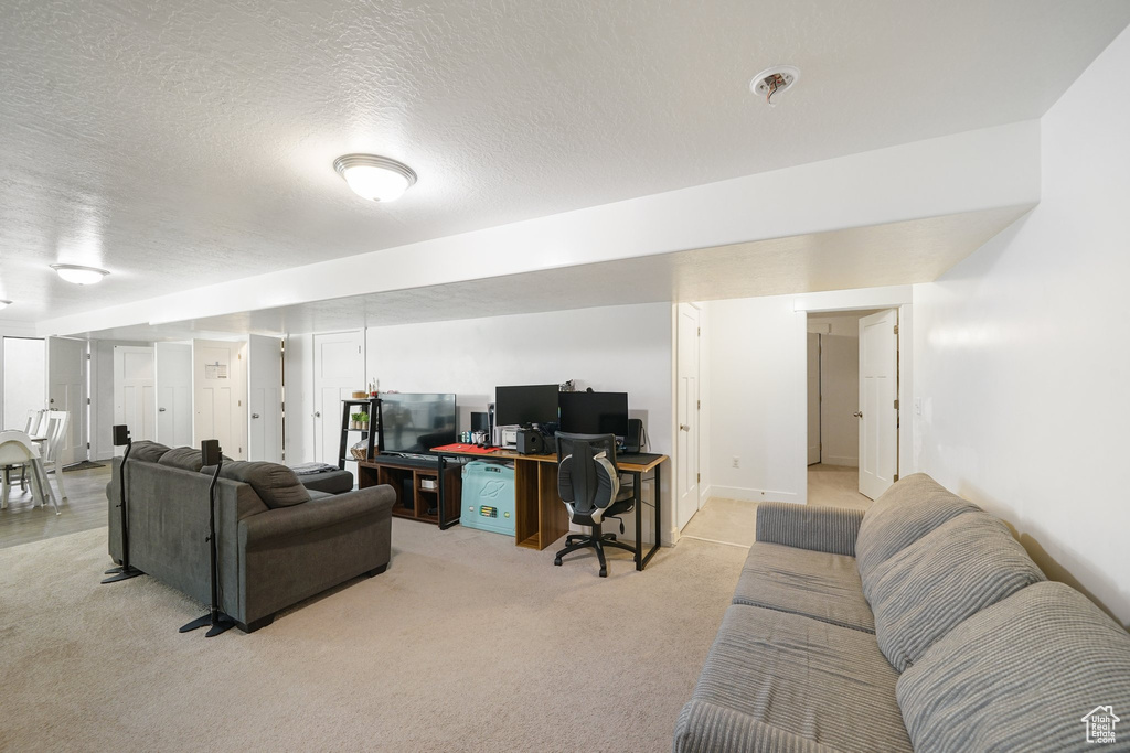 Living area with a desk, a textured ceiling, and light carpet