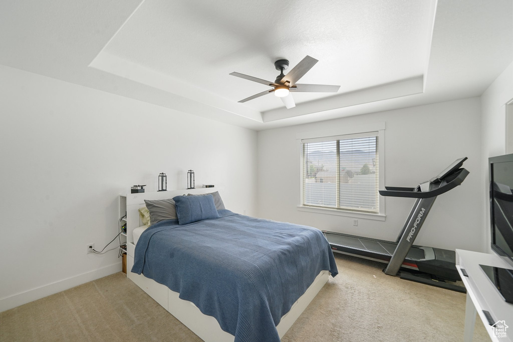 Bedroom featuring a tray ceiling, light colored carpet, and ceiling fan