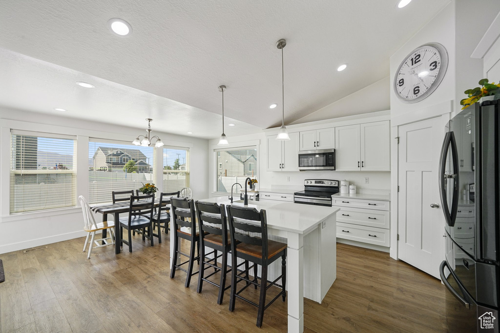 Kitchen featuring appliances with stainless steel finishes, light countertops, white cabinetry, a kitchen breakfast bar, and vaulted ceiling