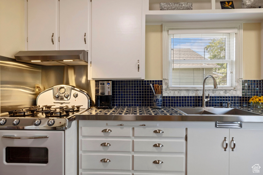 Kitchen featuring stainless steel gas range oven, wall chimney exhaust hood, white cabinetry, and backsplash