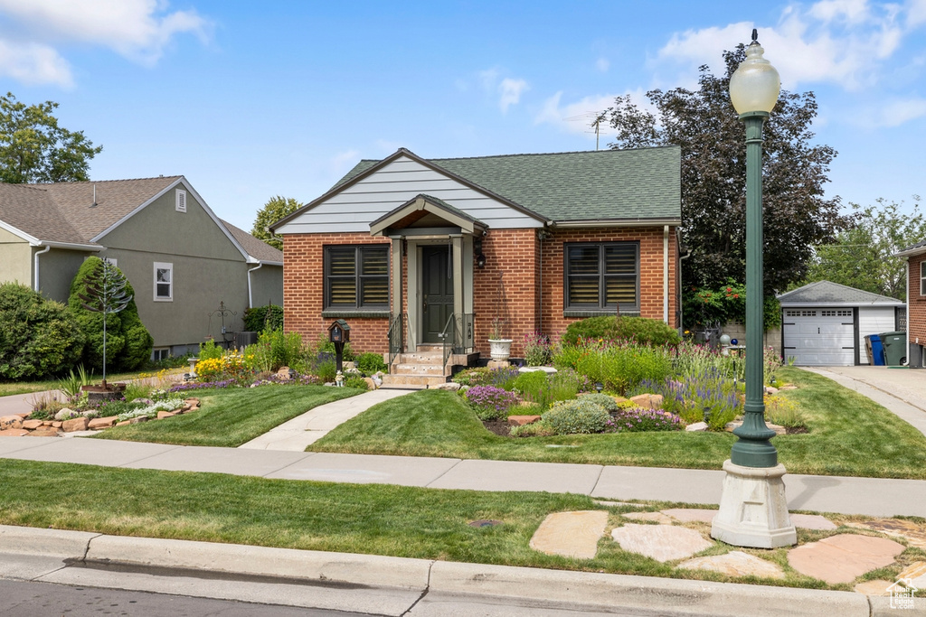 View of front of home featuring brick siding, an outdoor structure, a front yard, a garage, and a shingled roof