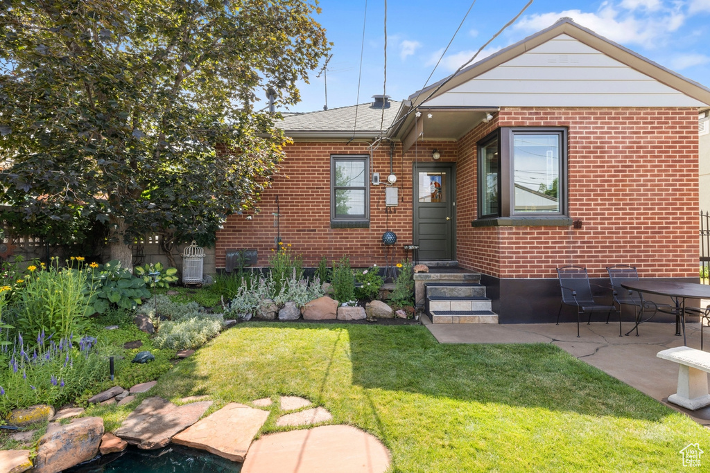 View of front of house featuring brick siding, a front yard, and a patio area