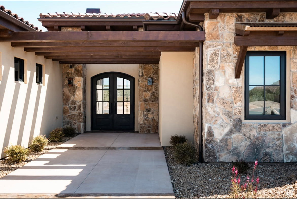 View of exterior entry featuring stone siding, french doors, a tile roof, and stucco siding