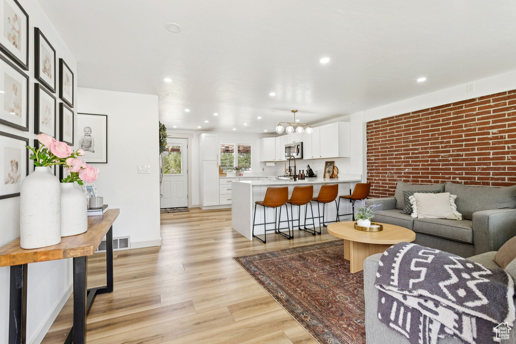 Living area featuring recessed lighting, light wood-style flooring, brick wall, and a chandelier