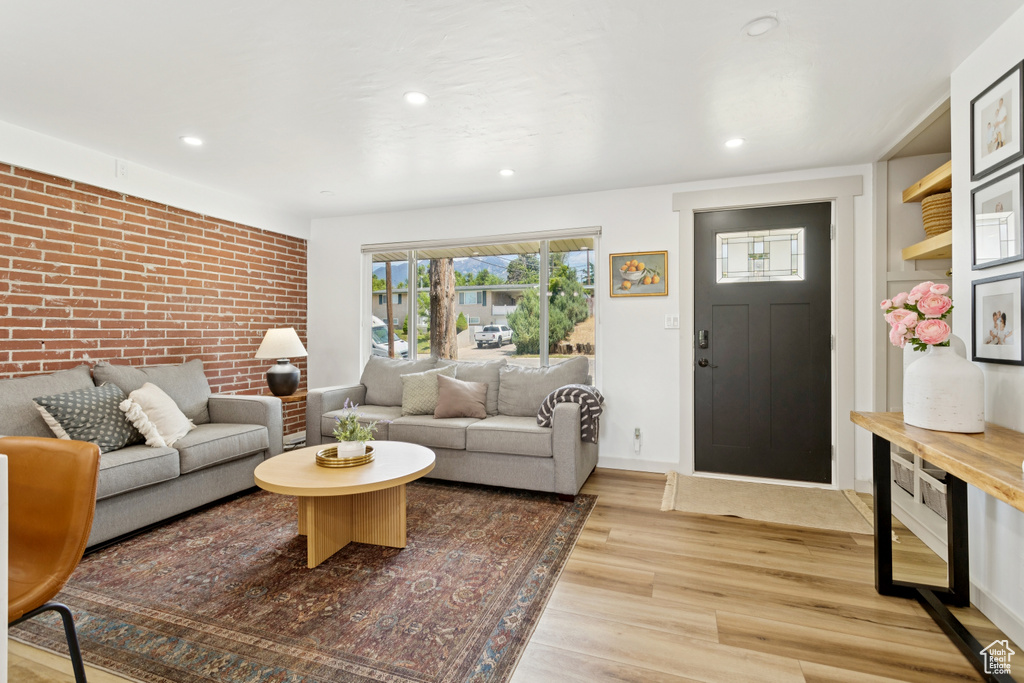 Living area featuring light wood finished floors, recessed lighting, and brick wall
