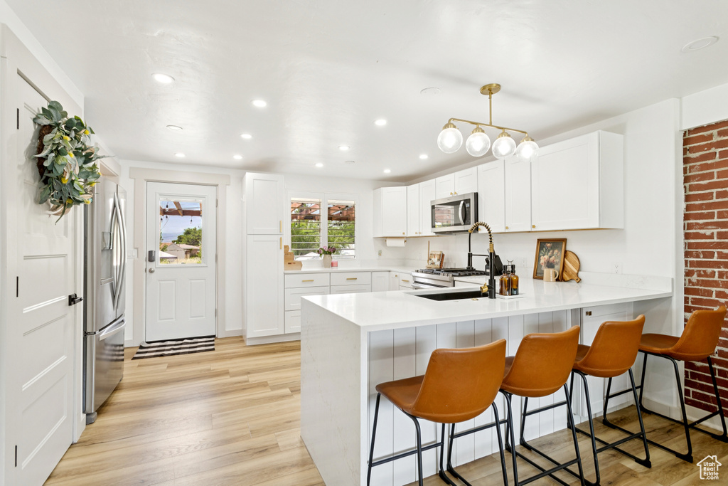 Kitchen with appliances with stainless steel finishes, a peninsula, a breakfast bar area, light wood-style flooring, and recessed lighting