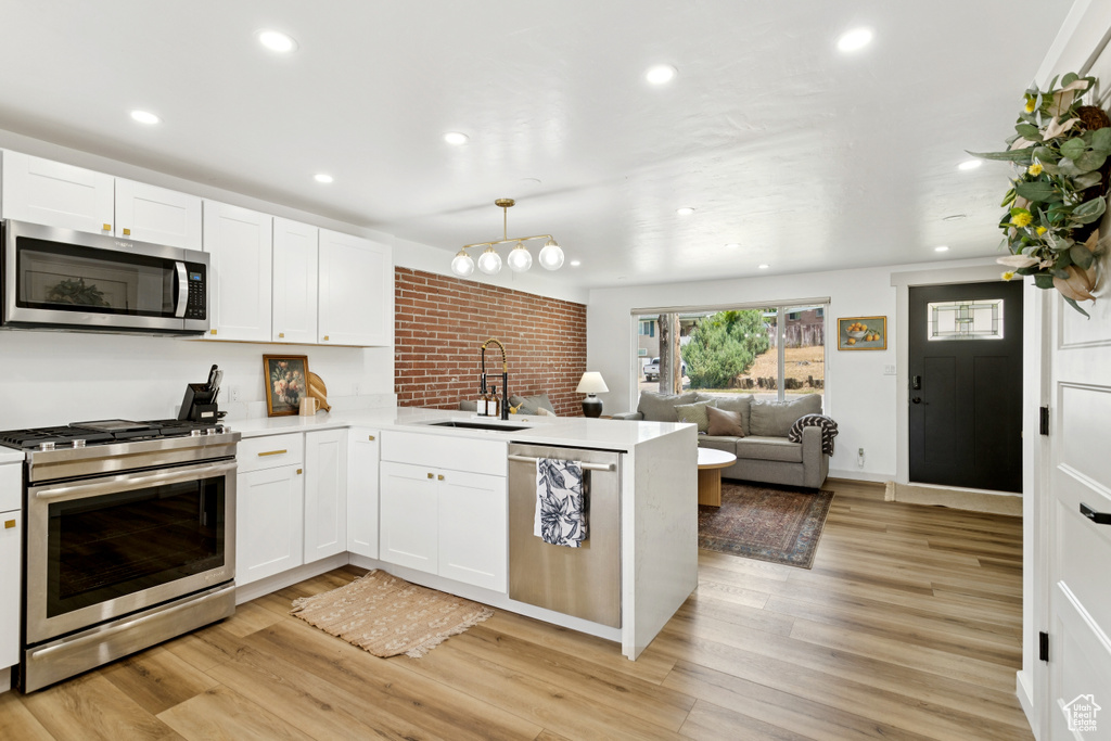 Kitchen with stainless steel appliances, a peninsula, open floor plan, white cabinetry, and light wood-style flooring