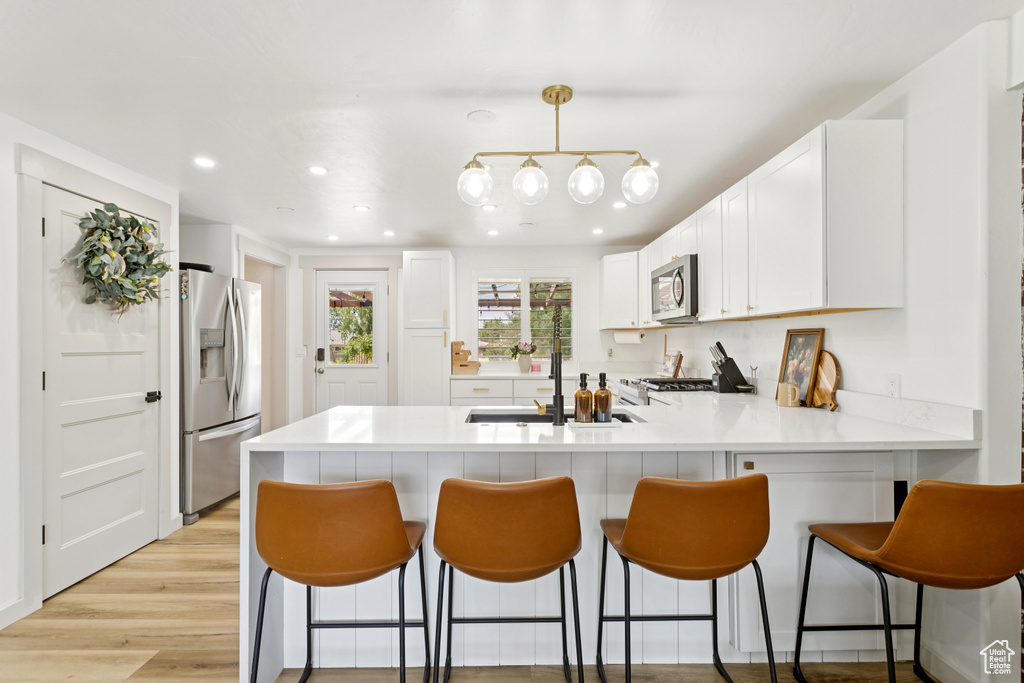 Kitchen featuring stainless steel appliances, a peninsula, light countertops, white cabinets, and a breakfast bar area