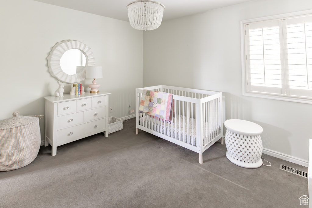 Carpeted bedroom featuring a chandelier and a nursery area