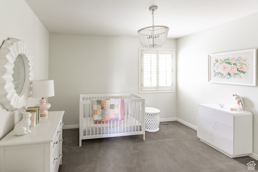 Carpeted bedroom featuring a chandelier and a nursery area