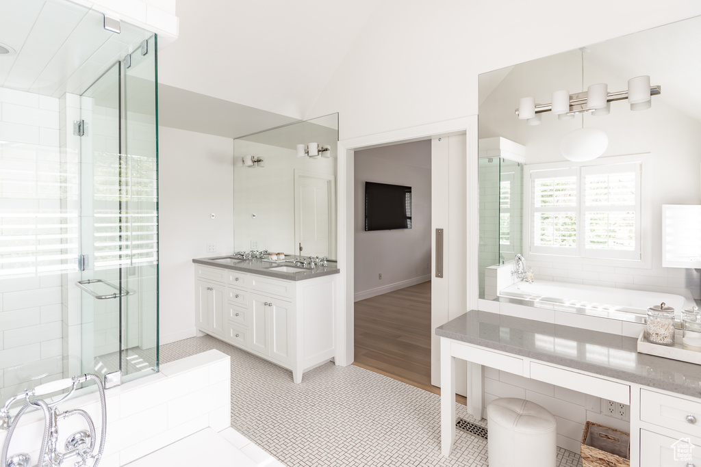 Bathroom featuring lofted ceiling, double vanity, a stall shower, a bath, and tile patterned flooring