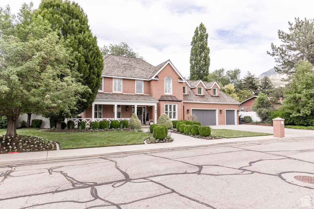 Traditional-style house with concrete driveway, covered porch, a front yard, a garage, and brick siding