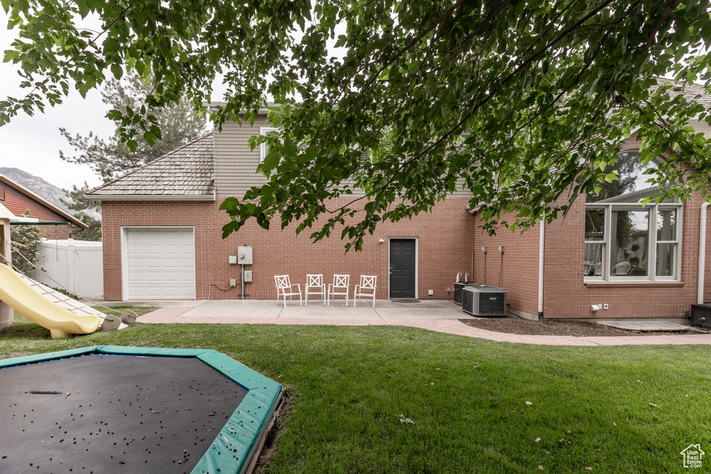 Rear view of property with brick siding, a patio area, a playground, and an attached garage