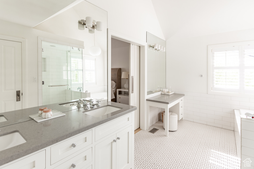 Bathroom featuring double vanity, healthy amount of natural light, a bath, a shower with door, and tile walls