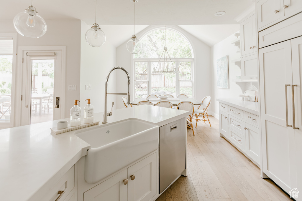 Kitchen featuring lofted ceiling, light wood finished floors, stainless steel dishwasher, light countertops, and hanging light fixtures