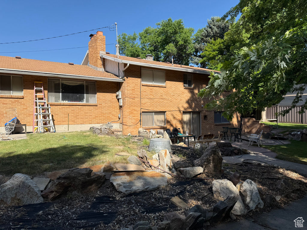 Rear view of property with brick siding, a chimney, a yard, and a patio
