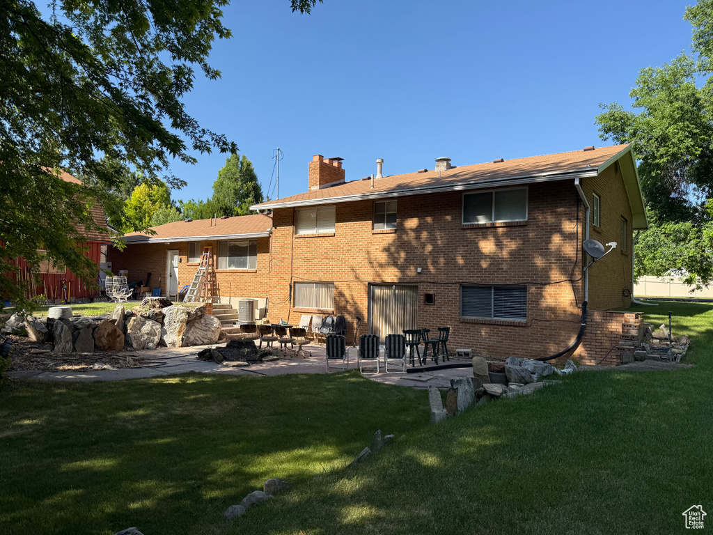 Rear view of property featuring a chimney, a patio area, a yard, and brick siding