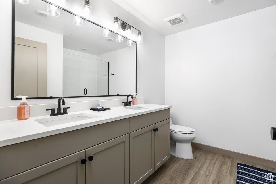 Bathroom with double vanity, wood finished floors, and an enclosed shower