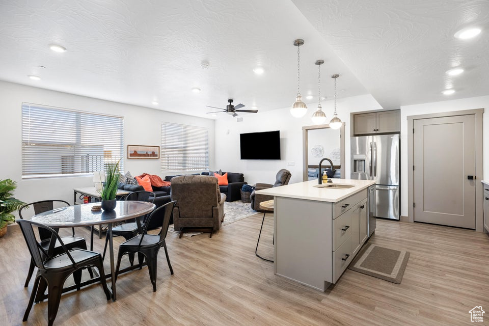 Kitchen featuring stainless steel fridge, gray cabinets, light wood-style flooring, a breakfast bar, and recessed lighting