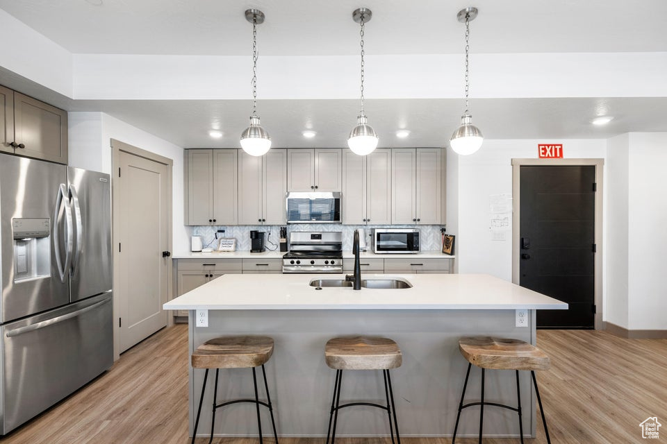 Kitchen featuring stainless steel appliances, light wood-style flooring, tasteful backsplash, and a kitchen bar