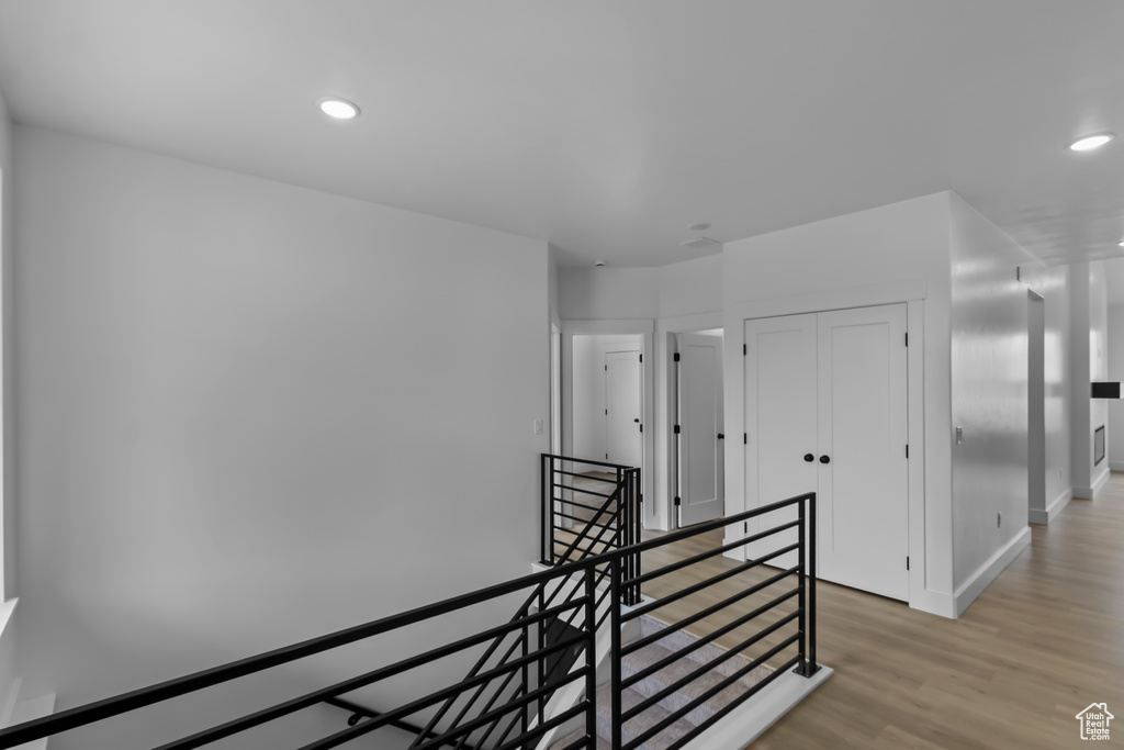 Corridor with an upstairs landing, light wood finished floors, and recessed lighting