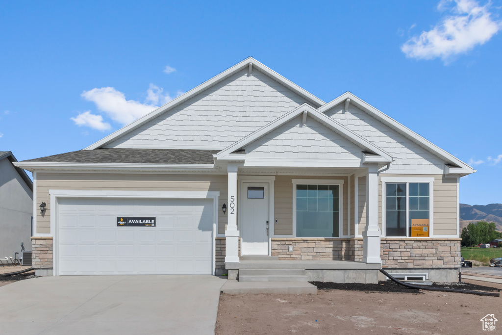 Craftsman inspired home featuring stone siding, a porch, concrete driveway, and an attached garage