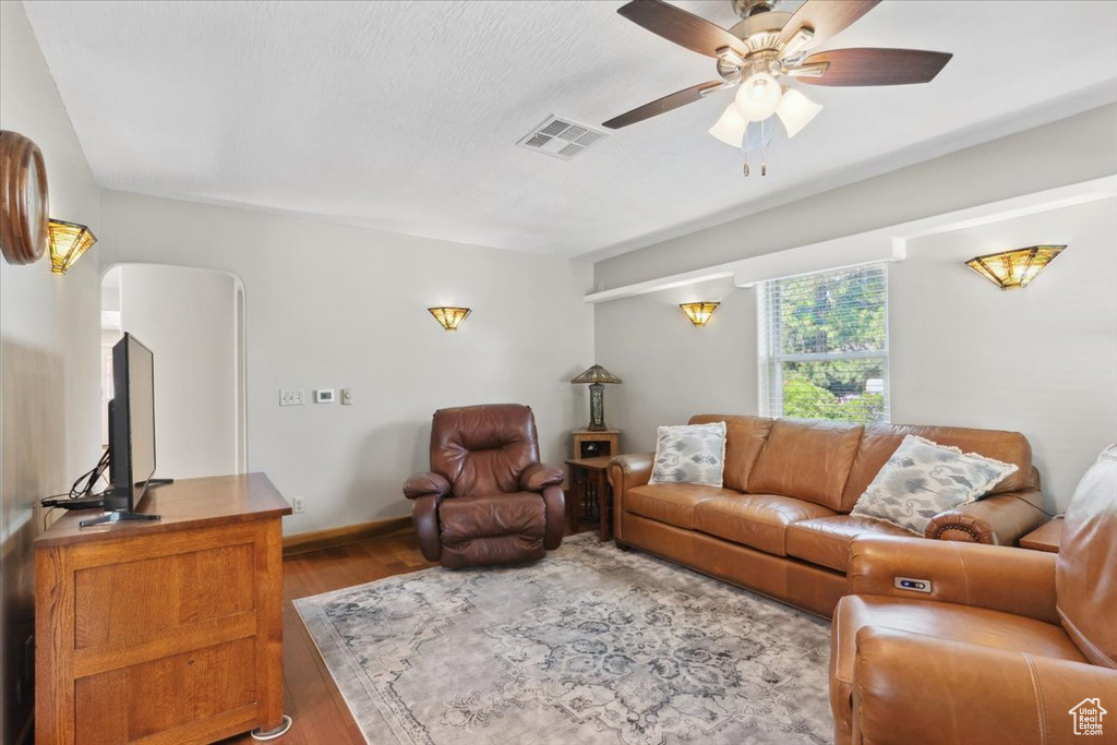 Living area with ceiling fan, wood finished floors, and arched walkways