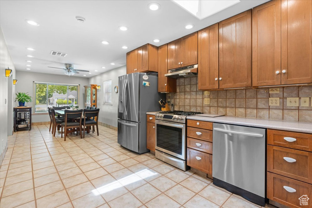 Kitchen featuring appliances with stainless steel finishes, light countertops, under cabinet range hood, brown cabinets, and recessed lighting