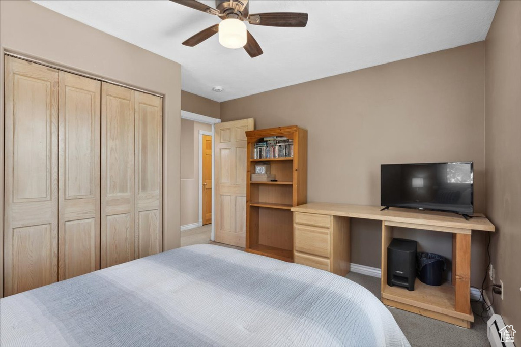 Carpeted bedroom featuring a baseboard radiator, an office area, a closet, and ceiling fan