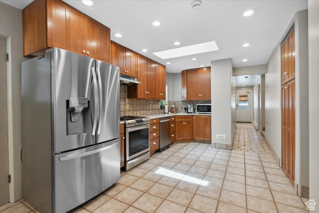 Kitchen with stainless steel appliances, light countertops, backsplash, under cabinet range hood, and light tile patterned flooring