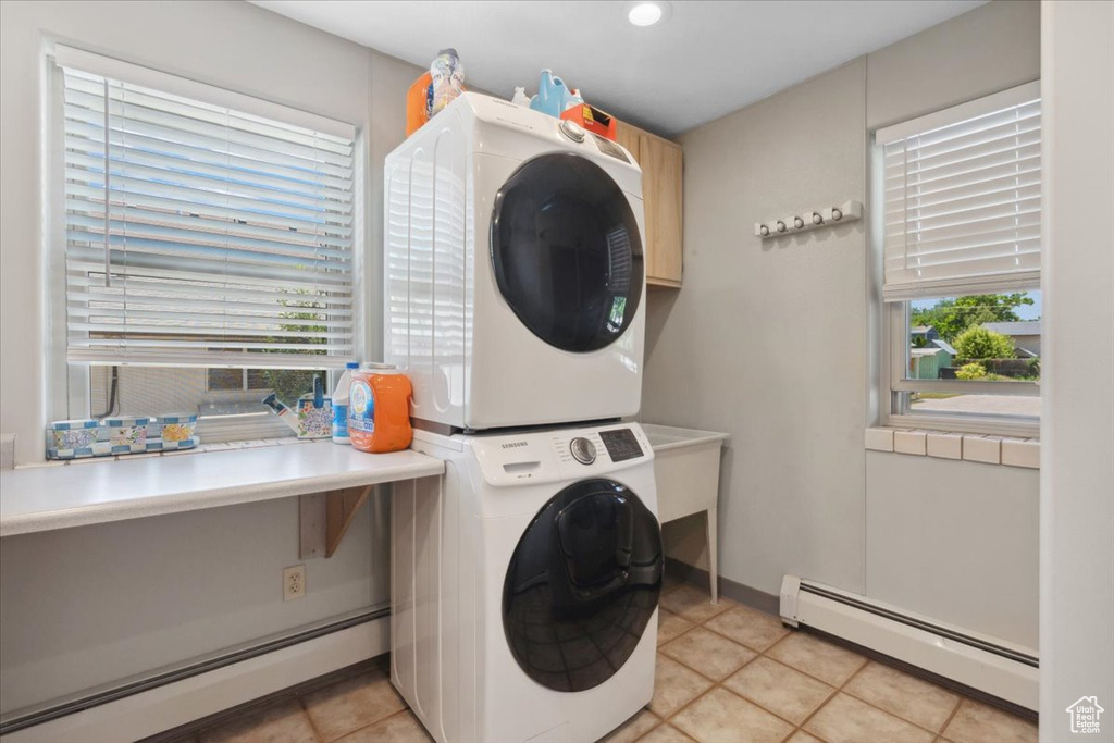 Laundry area featuring baseboard heating, stacked washer and clothes dryer, cabinet space, and light tile patterned floors