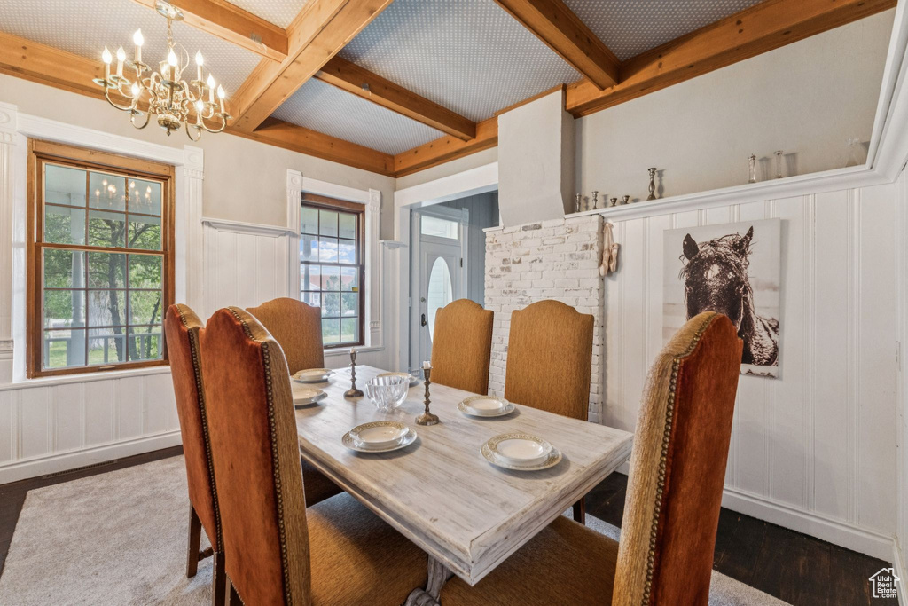 Dining area with wood finished floors, a decorative wall, beamed ceiling, a chandelier, and coffered ceiling