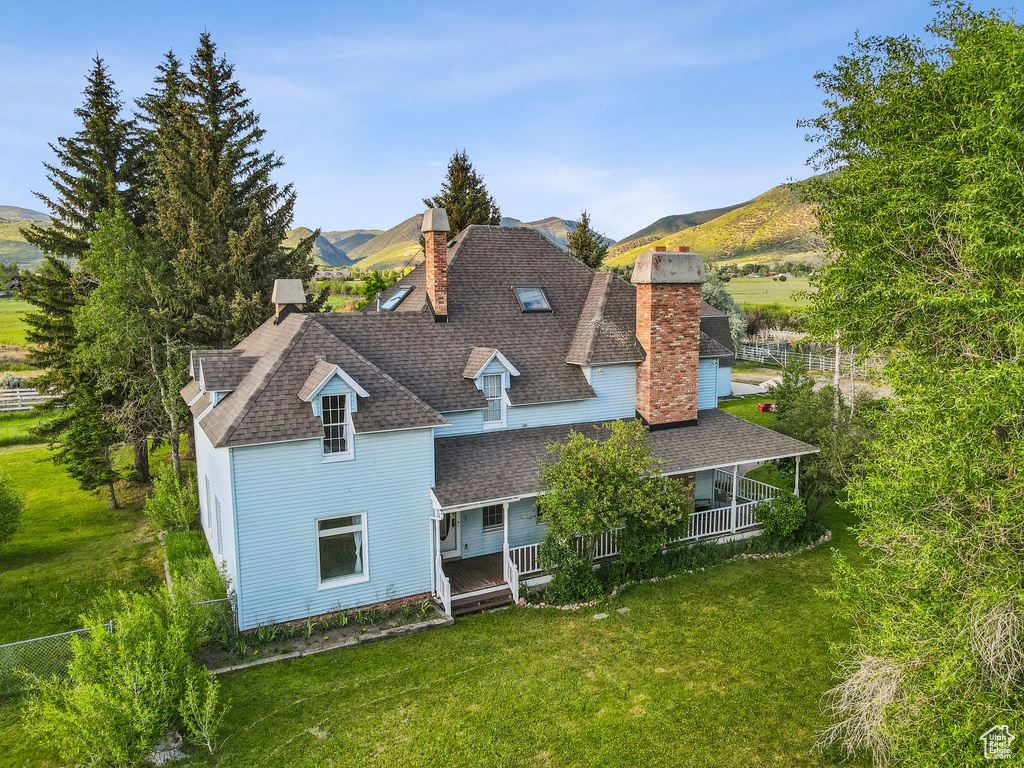 Back of house with a chimney, a lawn, a shingled roof, a porch, and a mountain view