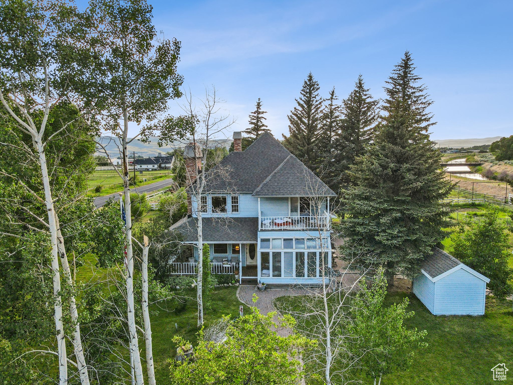 Back of property with a balcony, a chimney, a shingled roof, a sunroom, and a lawn