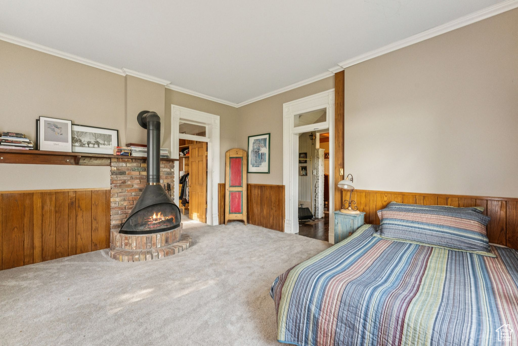 Carpeted bedroom with a wood stove, a wainscoted wall, crown molding, and wood walls