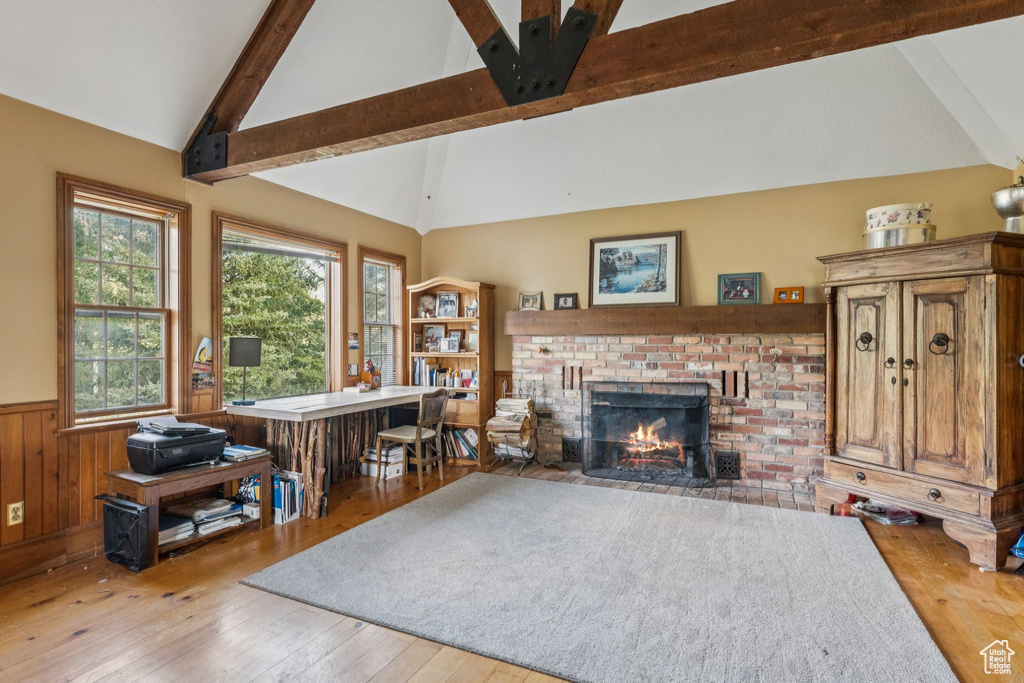 Living area with wainscoting, wood-type flooring, a brick fireplace, beam ceiling, and high vaulted ceiling