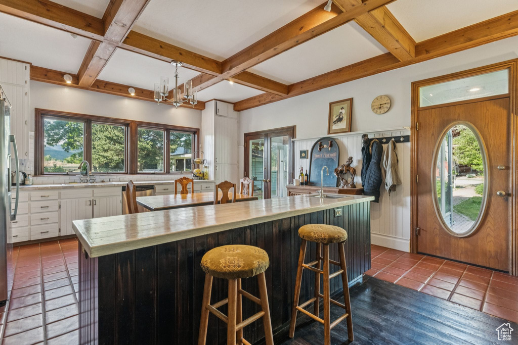 Kitchen with coffered ceiling, beam ceiling, white cabinetry, a kitchen island, and a chandelier