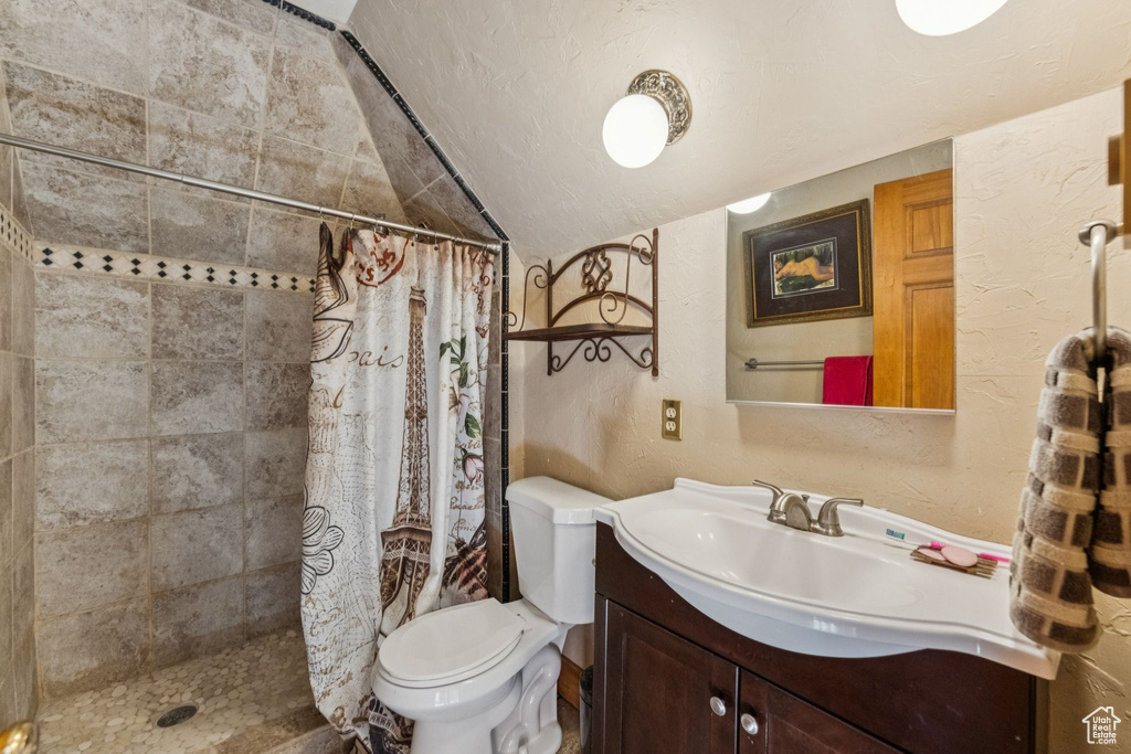 Bathroom featuring a textured wall, vaulted ceiling, vanity, a tile shower, and a textured ceiling