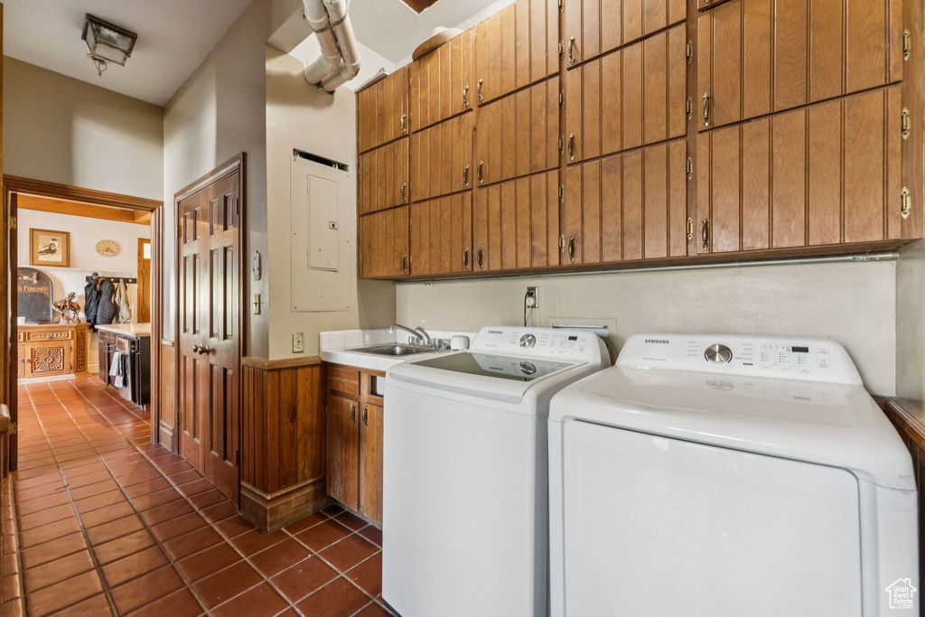 Laundry room with cabinet space, washer and dryer, dark tile patterned floors, and electric panel