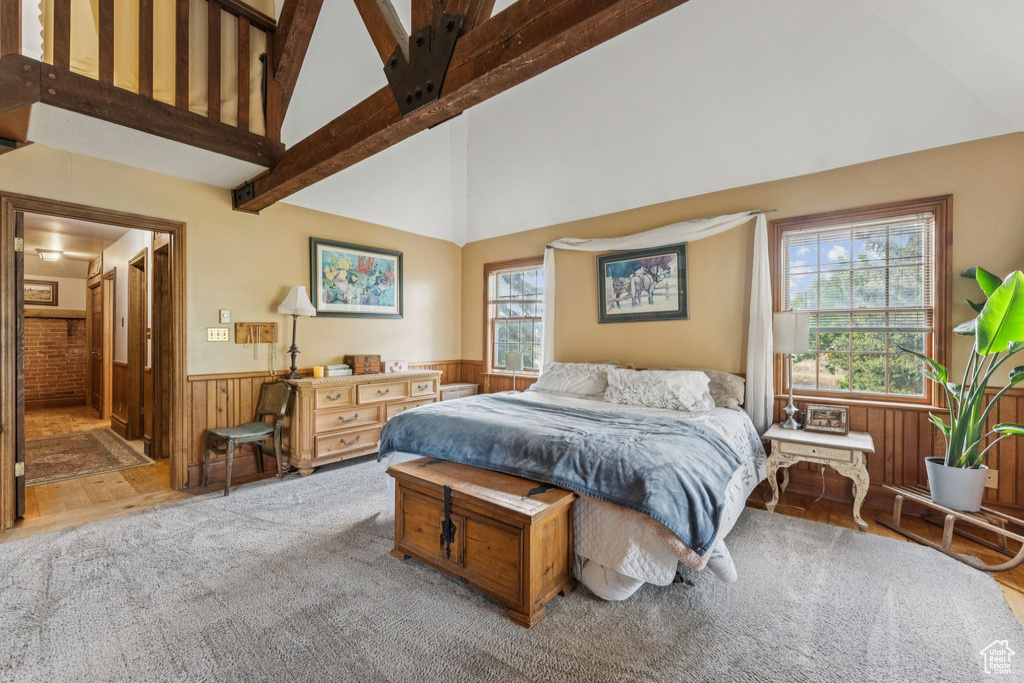 Bedroom featuring a wainscoted wall, wooden walls, high vaulted ceiling, carpet floors, and beamed ceiling
