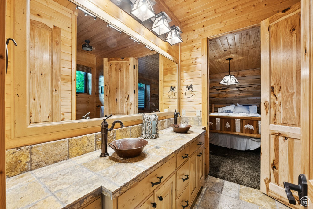 Full bathroom featuring stone tile floors, double vanity, wood ceiling, wooden walls, and ensuite bathroom
