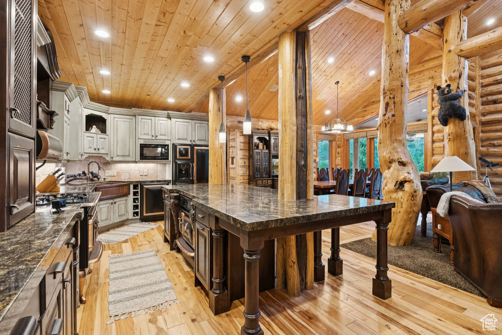 Kitchen with black microwave, refrigerator, light wood-style flooring, a kitchen bar, and a large island