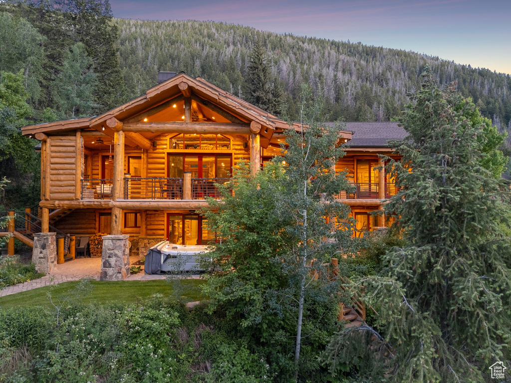 Back of property featuring a forest view, log exterior, a balcony, and a patio